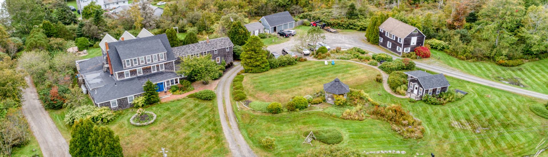 Exterior aerial view of property surrounded by green grass, bushes and trees