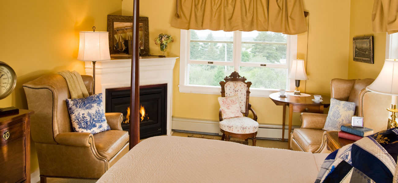 Gold room with pink bedspread, tan wingback chair and fire in the fireplace.