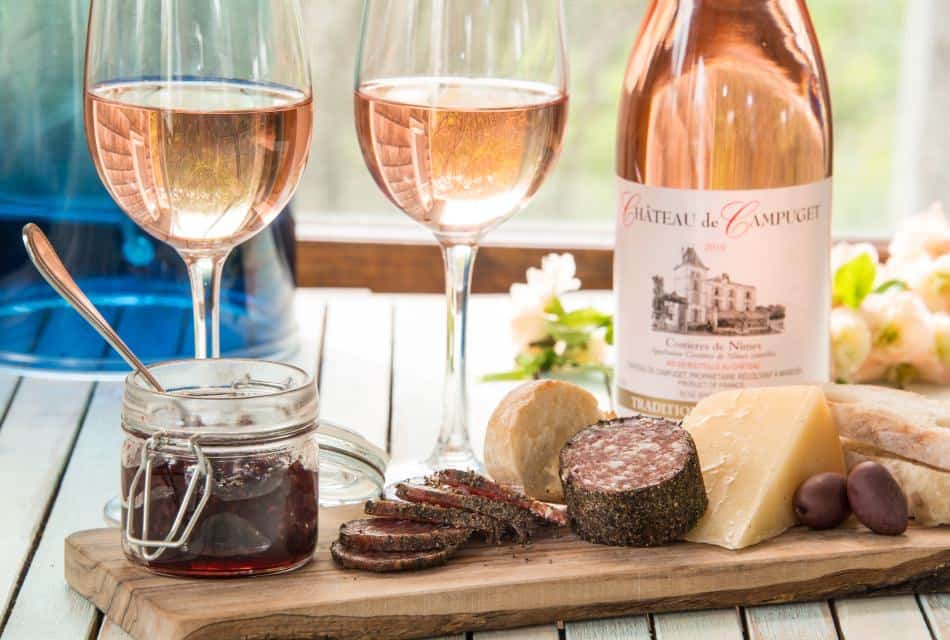 Close up view of wine filled glasses, bottle of wine, and charcuterie board with cheese, meat, bread, and jam