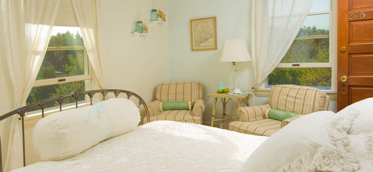 Iron bed with white pillows and duvet. Two brown fabric recliners in the corner.